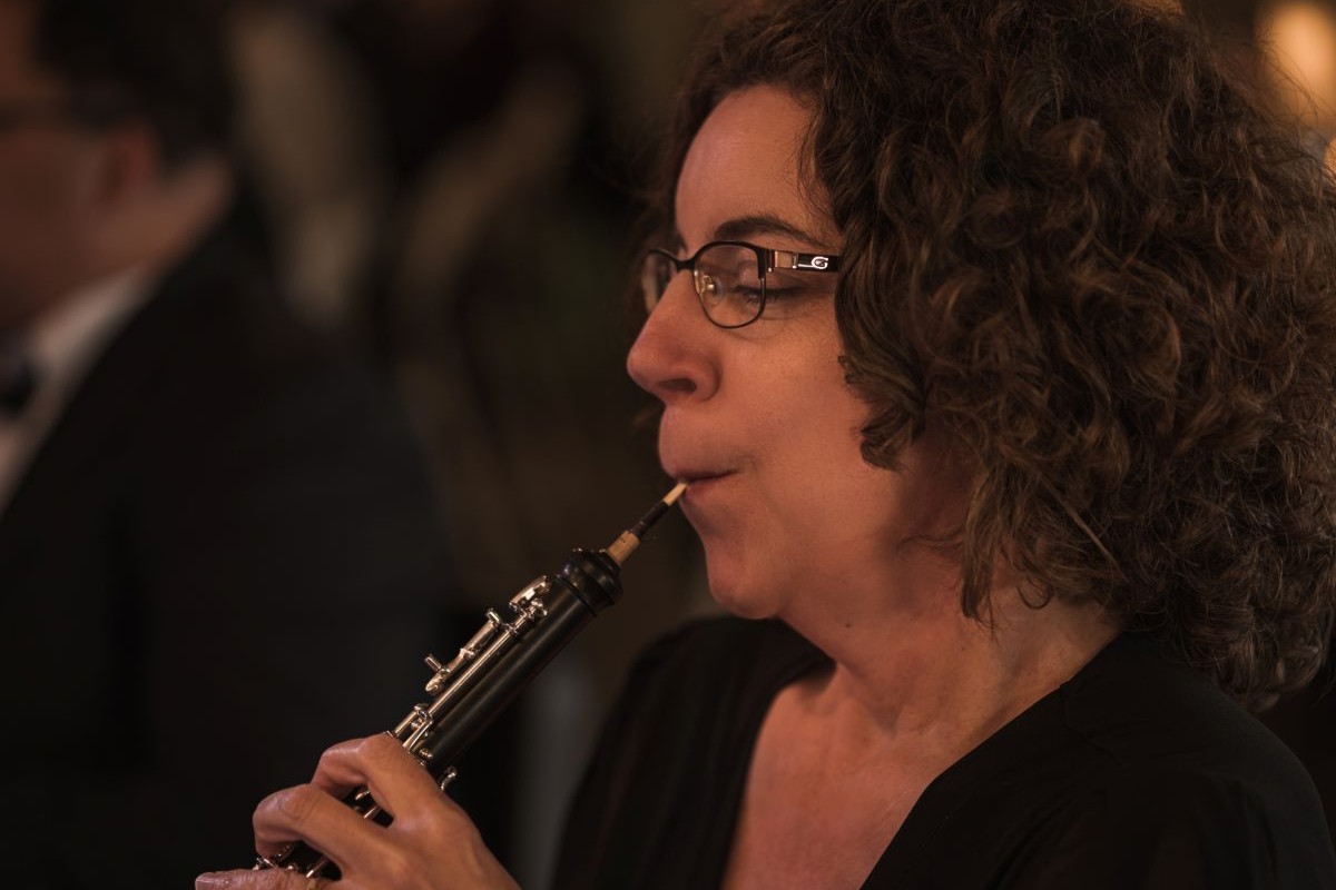 A close up of an adult female sitting playing the oboe in an orchestra